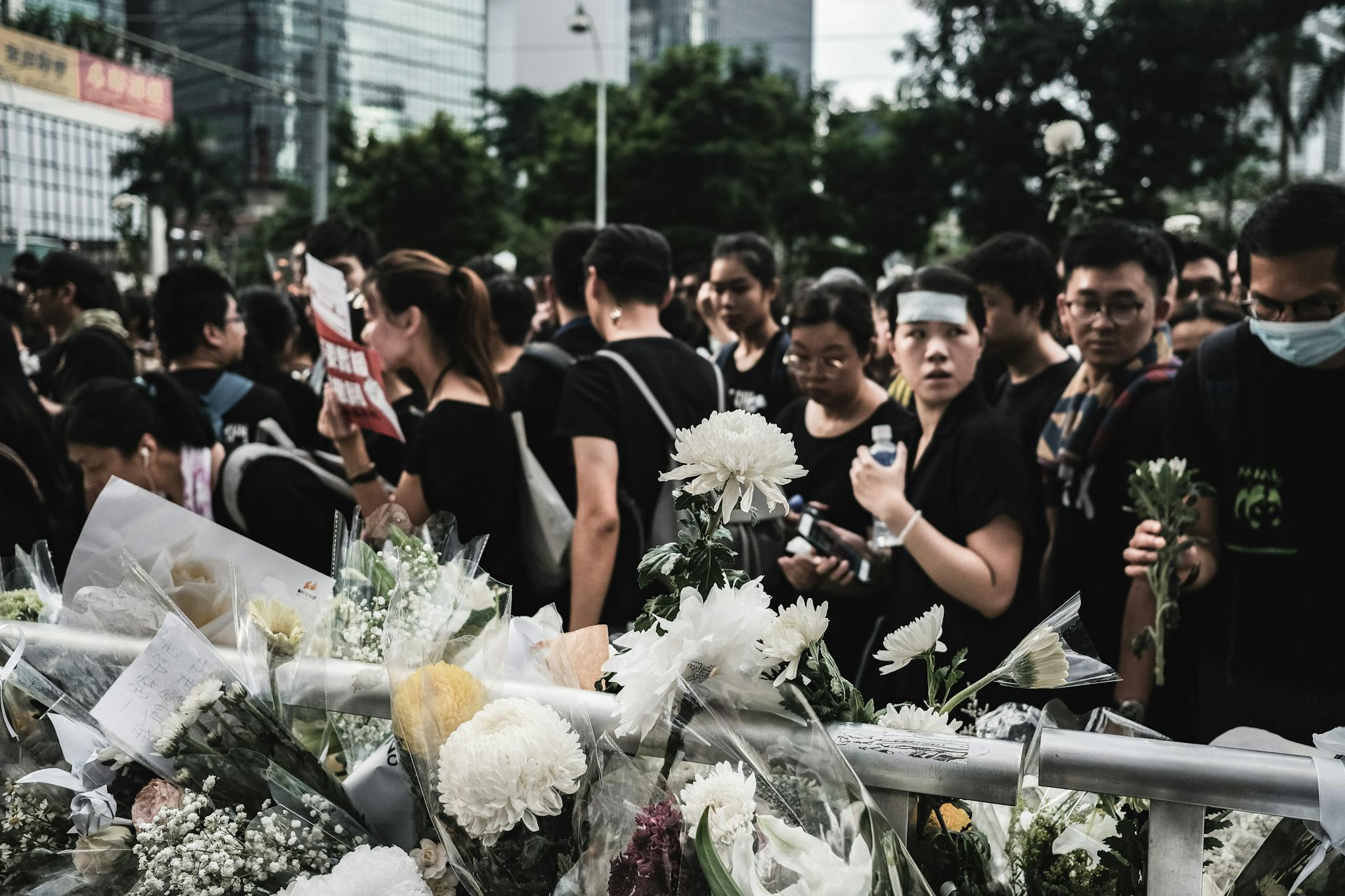 A solemn crowd in Hong Kong gathers around a floral memorial, wearing black for unity.